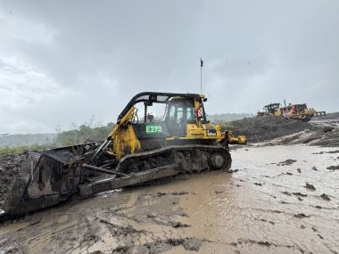 Yağmurlu bir günde çamurlu arazide çalışan güçlü buldozer zorlu bir ortamda ağır inşaat ekipmanları ve toprak taşıma operasyonları sergiliyor..