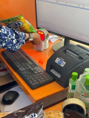 Bir işçi, klavye ve makbuz yazıcısının yanında bir barkod tarayıcısı kullanarak bakkal kasasında erzak taraması yapar.