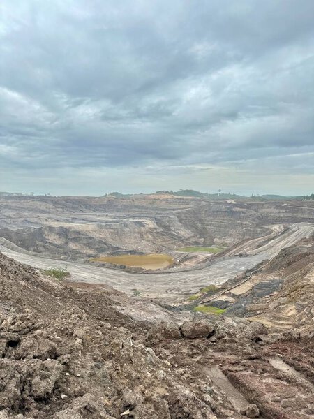 Vast open-pit mine under a cloudy sky.  Shows the scale of industrial mining and its impact on the environment. Resource extraction, earthworks, industrial landscape.