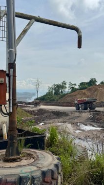 Ağır yük taşıyan bir kamyon, yeni inşa edilmiş bir sanayi bölgesinde malzeme taşıyor. Sahne endüstri ve doğanın kesişimlerini gösteriyor, gökyüzü bulutlu..