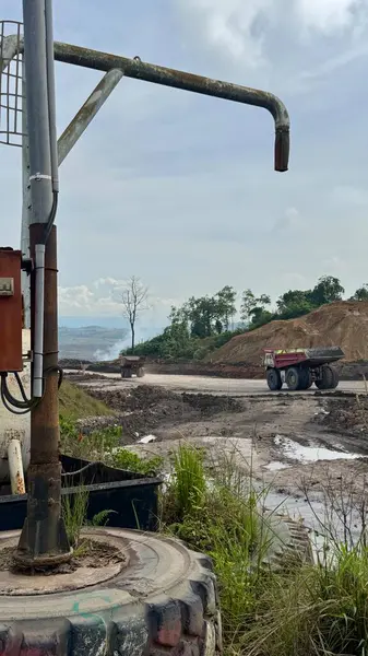 Ağır yük taşıyan bir kamyon, yeni inşa edilmiş bir sanayi bölgesinde malzeme taşıyor. Sahne endüstri ve doğanın kesişimlerini gösteriyor, gökyüzü bulutlu..