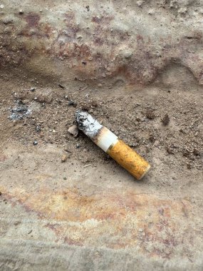 Cigarette butt discarded on dirty ground.  Environmental pollution, littering, tobacco waste, public hygiene issues.  Close-up view of carelessly disposed waste.