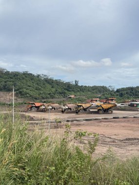 Kömür madeni kamyonları Lush Green Hills 'in yakınına park etmiş Bulutlu bir gökyüzünün altında