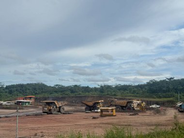 Ağır makineler, yemyeşil bitki örtüsü yakınlarında bulutlu bir gökyüzünün altında tropikal bir taş ocağında çalışır..