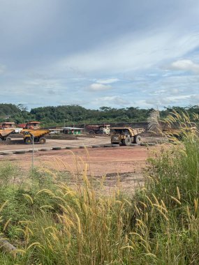 Madencilik operasyonunda ağır makineler yeşil çimenler ve parçalı bulutlu gökyüzü ile pitoresk bir manzara oluşturuyor. Endüstriyel madencilik ekipmanları iş başında.