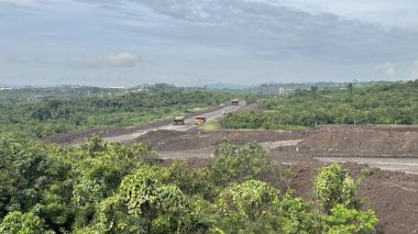 Bereketli yeşil tropikal ormanın ortasındaki bir otoyol şantiyesinin havadan görünüşü. Yol gelişimi doğal manzarayı etkiliyor.