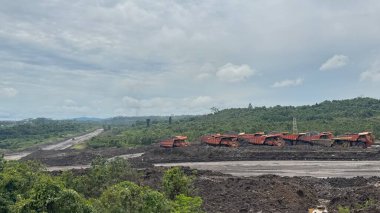 Bulutlu bir gökyüzünün altındaki yemyeşil tepelerin ortasında bir otoyol yakınında madencilik operasyonu