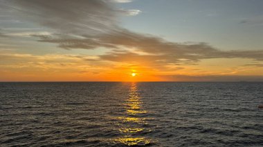Sakin bir okyanusun üzerinde nefes kesici bir gün batımı. Güneş ufkun altına batar ve suyun üzerine altın bir parıltı saçar. Bulutlar sıcak renklerle gökyüzünü boyar. Sakin ve huzurlu..