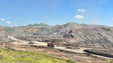 Mavi gökyüzü altında ağır makineler ve çevresel etkiyi gösteren büyük bir açık maden operasyonu