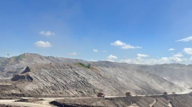 Dinamik kamyonlar, parlak mavi gökyüzünün altındaki büyük bir açık maden ocağından malzeme taşıyor.