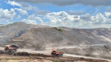 Heavy mining trucks transport coal in an open pit mine under a blue sky, showcasing the power of industry and resource extraction across a vast landscape.