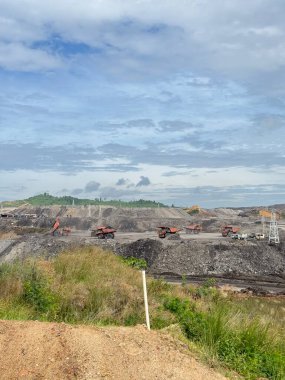Open pit coal mine with heavy machinery under a cloudy sky showcasing resource extraction and environmental impact in a natural setting