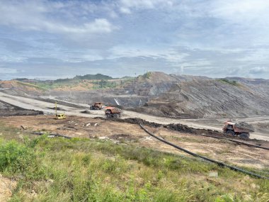 Powerful trucks transporting materials at an open pit mine site under a vast, cloudy sky showcasing industry and environmental impact