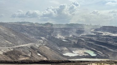 Dramatik açık maden sahası, doğal kaynak çıkarma ve bulutlu gökyüzü altında çevresel etkiyi, sanayi ve doğanın katıksız zıtlığını gösteriyor.