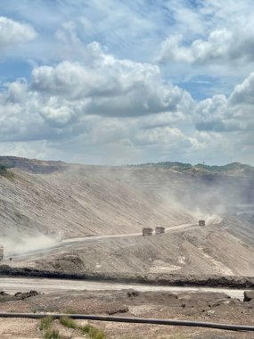 Dev kamyonlar, dramatik bulutlu gökyüzü altında, endüstriyel çıkartma sahasında geniş bir açık çukur mayını boyunca Dünya 'yı sürüklüyor.