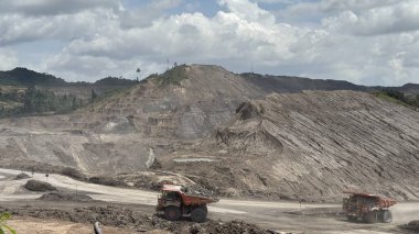 Massive open-pit mine operations with heavy machinery excavating earth under a cloudy sky showcasing industrial scale extraction