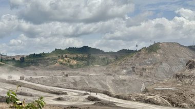 Vast open-pit mine operations with heavy machinery excavating earth under a dramatic cloudy sky, showcasing industrial extraction and large-scale construction.