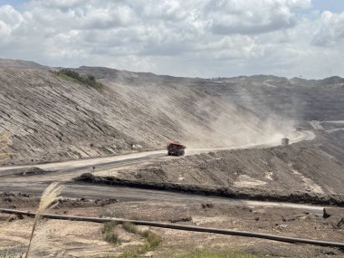 Muazzam maden kamyonları engin açık kömür madenlerinde tozlu yolları aşarak sisli bir yaz gökyüzünün altında endüstriyel çıkartma operasyonlarını gösteriyor..