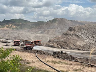 Massive open-pit coal mine operations with heavy machinery transporting materials under a vast, cloudy sky
