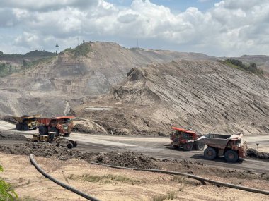 Massive haul trucks navigate a vast, rugged open-pit mine under a cloudy sky, transporting earth and minerals in a dynamic industrial landscape.