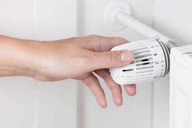 Isıtma radyatörünün ısısını ayarlayan bir kadın para biriktirmeye ve enerji tasarrufu yapmaya odaklanıyor. Daha soğuk aylarda dikkatli kaynak yönetimi ve maliyetli yaşamın önemi, ev giderlerini yönetme amaçlı eylemler