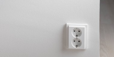 Beyaz bir duvara monte edilmiş çift elektrik prizinin yakın çekimi. Elektrik tüketimi ve enerji tasarruflarının farkında olmak, elektrik kullanımının verimli bir şekilde yönetilmesi ve günlük yaşamda atıkların azaltılması