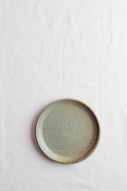 Yemek tabakları için arka plan olarak fotokopi alanı olan beyaz bir masa örtüsü üzerinde boş, eski model bir tabak.