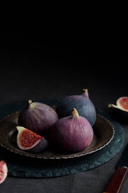 Taze olgun ve tatlı bir bütün ve mutfak bıçağıyla dilimlenmiş incirler ev mutfağının karanlık arka planında eski bir kırsal metal plaka üzerinde, fotokopi alanı ile dikey afiş