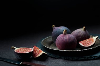 Taze olgun ve tatlı bir bütün ve mutfak bıçağıyla dilimlenmiş incir eski bir metal plaka üzerinde ev mutfağının karanlık arka planında, fotokopi alanı ile yatay afiş