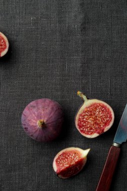 Koyu arkaplanda taze incir, bütün ve dilimlenmiş, lezzetli ve tatlı incirler, siyah masa örtüsü üzerinde bir mutfak bıçağı, dikey üst görünüm afişi ve fotokopi alanı.