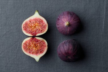 Koyu arkaplanda taze incir, bütün ve dilimlenmiş, lezzetli ve tatlı incirler, siyah masa örtüsü üzerinde bir mutfak bıçağı, dikey üst görünüm afişi ve fotokopi alanı.