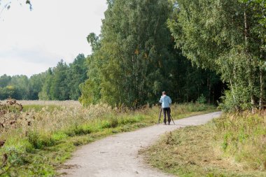 Espoo, Finlandiya, 25.08.2024 - Adam, Suomenoja, Finnoo 'da kuşları ve diğer hayvanları gözlemlemek için kamera kullanıyor. Gündüz vakti parkta vahşi doğa fotoğrafçısı. Profesyonel dijital kamera tripoda sabitlendi. Çalışma süreci. Arka plan.