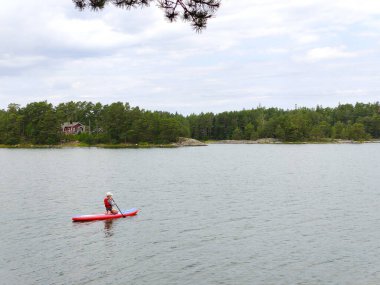 Baltık Denizi 'nde sörf tahtasında kürek çeken küçük bir çocuk, Finlandiya Körfezi, çocuk tatili, Finlandiya' da aktif yaz tatili.