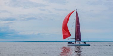 Açık denizde küçük dalgalar halinde yelken açıyorlar. Yelkenli sancaklı deniz manzarası afişi. Kırmızı yelkenli yelkenli altında yelken açan yat, yat yarışına katılıyor.