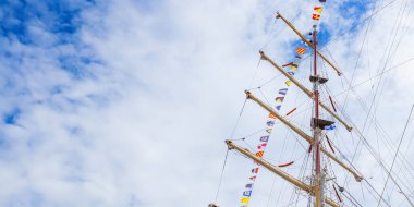 Mavi güneşli bir gökyüzü ve bulutlarda bayrak bayrağını dalgalandıran yelkenli gemi direği. Renkli iplerle donatılmış eski bir gemi. Pankart