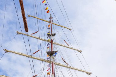 Mavi güneşli bir gökyüzü ve bulutlarda bayrak bayrağını dalgalandıran yelkenli gemi direği. Renkli iplerle donatılmış eski bir gemi. Pankart