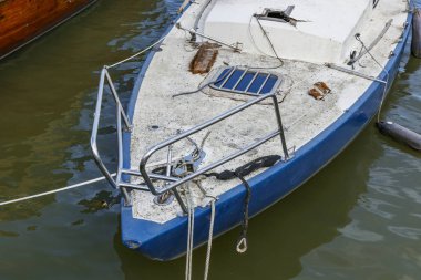 Denizde terk edilmiş, eski, kirli, bakımsız bir yelkenlinin kapısına yakın açık mavi ve beyaz yelkenli, kırık direkli.