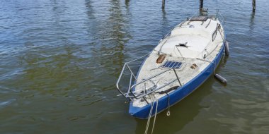 Denizde terk edilmiş, eski, kirli, bakımsız bir yelkenlinin kapısına yakın açık mavi ve beyaz yelkenli, kırık direkli.