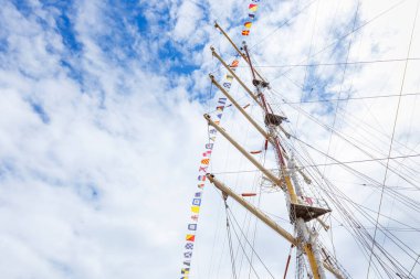 Mavi güneşli bir gökyüzü ve bulutlarda bayrak bayrağını dalgalandıran yelkenli gemi direği. Renkli iplerle donatılmış eski bir gemi. Pankart
