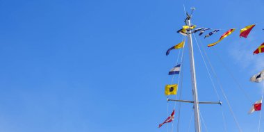 Uluslararası denizcilik bir bayrak direğinde bayraklar ve arkasında mavi bir gökyüzü olan yelkenli bir gemide direkler. Pankart