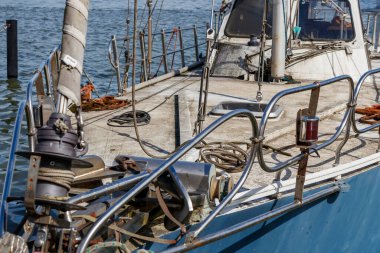 Denizde terk edilmiş, eski, kirli, bakımsız bir yelkenlinin kapısına yakın açık mavi ve beyaz yelkenli, kırık direkli.