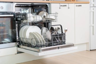 Tam yük bulaşık makinesi. Temiz bulaşıklar ve çatal bıçak takımı. Beyaz modern mutfakta kolaylık