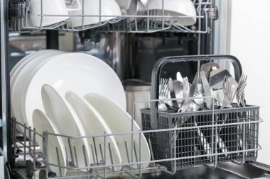 Temiz sofra takımı ve beyaz porselen tabakları olan açık bir bulaşık makinesi. Mutfakta modern teknolojiler var.