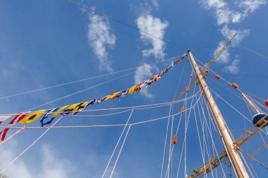 Mavi güneşli bir gökyüzü ve bulutlarda bayrak bayrağını dalgalandıran yelkenli gemi direği. Renkli iplerle donatılmış eski bir gemi. Pankart