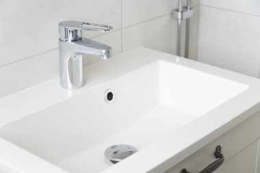 Beyaz modern banyodaki musluktan damlayan bir damla saf su. Temiz musluk suyu konsepti. Doğal kaynakların akıllıca kullanımı.