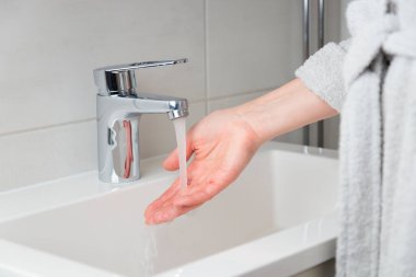 Akış musluğuyla su ısısını deneyen bir kadınla pankart. Krom musluktan su akıyor. Banyo tesisatı. Vücut bakımı ve hijyen kavramı