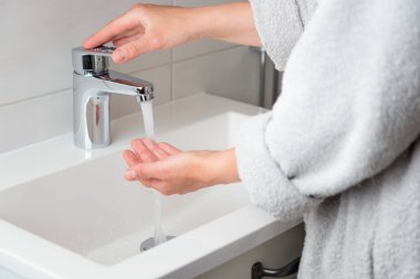 Kadın musluğu açıp su ısısını denerken afiş. Krom musluktan su akıyor. Banyo tesisatı. Vücut bakımı ve hijyen