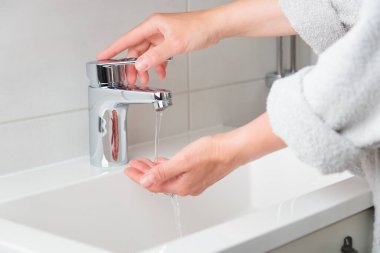 Kadın pankartı su akışı musluğunu açıp kapıyor ve su sıcaklığını dolduruyor. Krom musluktan su akıyor. Banyo tesisatı. Su kaynakları kavramını kullanarak