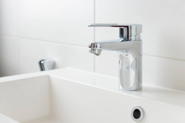 Beyaz modern banyodaki musluktan damlayan bir damla saf su. Temiz musluk suyu konsepti. Doğal kaynakların akıllıca kullanımı.