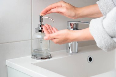 İç tuvalette el yıkama prosedürü için ilaç şişesinden sıvı sabun kullanan bir kadın görüntüsü. Kadın dezenfektan jeli ya da antibakteriyel temizleyici kullanıyor. Hijyen kavramı
